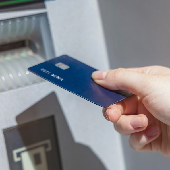 Damska dłoń wkładająca kartę płatniczą do bankomatu
